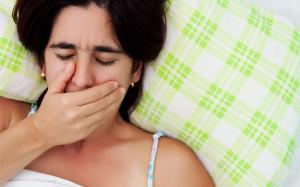 Woman lies in bed looking sick with hand over her mouth