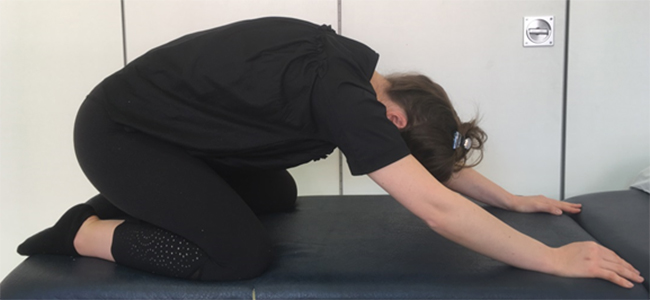 Woman on the floor sitting back on her heels with her face towards the floor and her arms outstretched in parallel beyond her head
