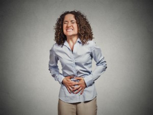Young woman with her hands on her stomach grimacing in pain