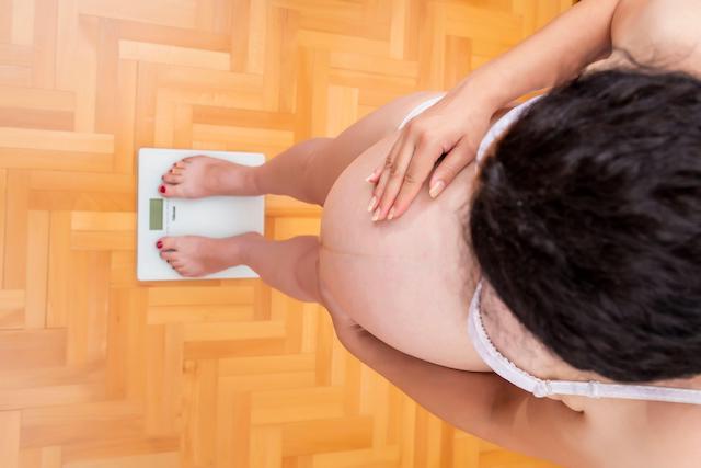 Pregnant woman standing on scale and measuring weight.